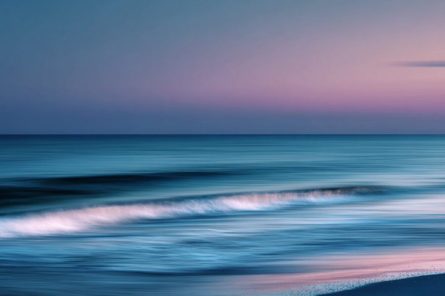 Soft, blurred waves roll across a pastel-colored shoreline at sunset, symbolizing the flow and serenity often associated with the question—what is tantra sex.