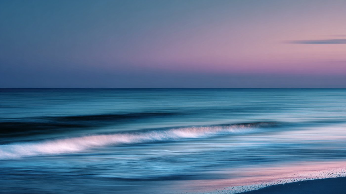 Soft, blurred waves roll across a pastel-colored shoreline at sunset, symbolizing the flow and serenity often associated with the question—what is tantra sex.