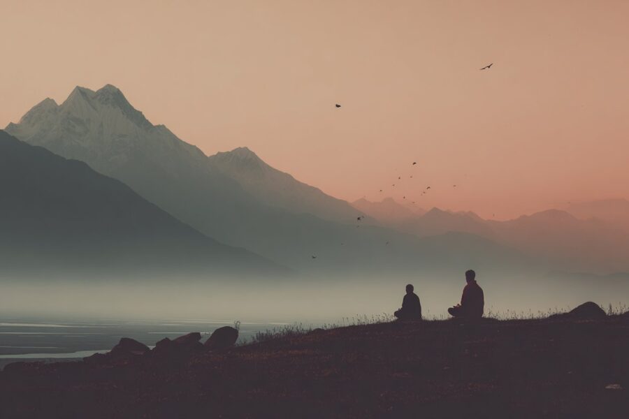 Two people meditate at sunrise in front of snow-capped mountains, reflecting the Secrets of Tantric Energy in stillness and nature.