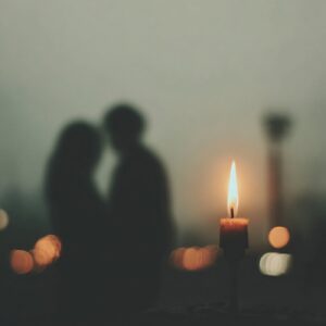 A glowing candle burns brightly with a blurred couple in the background, symbolizing intimacy and the Secrets of Tantric Energy.