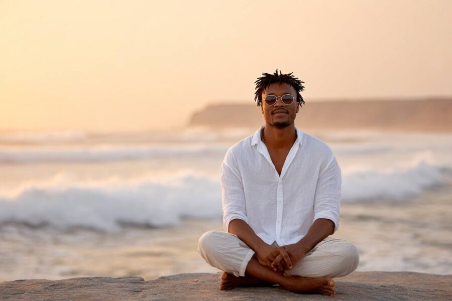 A man sits peacefully cross-legged on a beach at sunset, embodying calm presence and the reflective journey of tantra for singles.